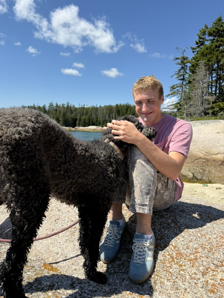 Joey sitting with a black dog on a rocky coastline